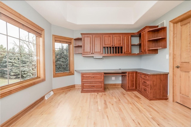 unfurnished office with built in desk, visible vents, light wood finished floors, and a tray ceiling