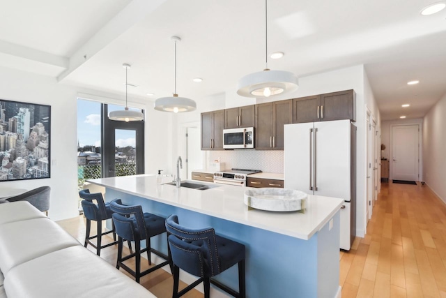 kitchen with a center island with sink, hanging light fixtures, a breakfast bar, and white appliances