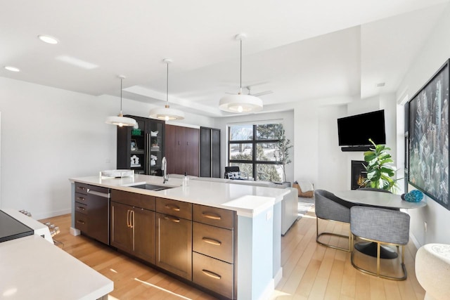 kitchen with sink, light wood-type flooring, dark brown cabinets, dishwasher, and a center island with sink