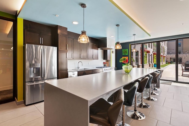 kitchen with sink, a kitchen island, a kitchen bar, hanging light fixtures, and stainless steel fridge