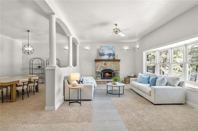 living area featuring decorative columns, baseboards, light colored carpet, ceiling fan, and a stone fireplace