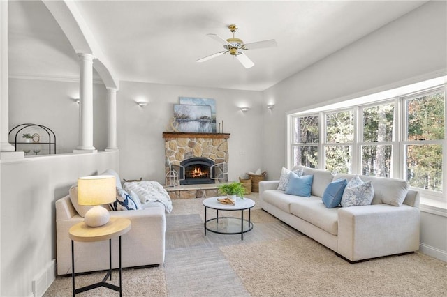 living room featuring a stone fireplace, light colored carpet, visible vents, a ceiling fan, and ornate columns