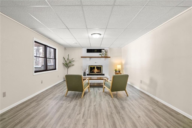 living area with a paneled ceiling, a large fireplace, wood finished floors, baseboards, and ornamental molding