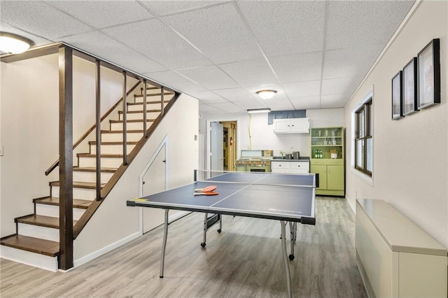recreation room with light wood-style floors, a paneled ceiling, and baseboards