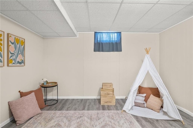 recreation room featuring baseboards, a drop ceiling, and wood finished floors