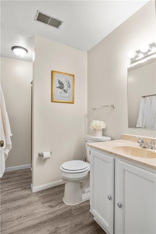 full bath featuring visible vents, toilet, vanity, wood finished floors, and baseboards
