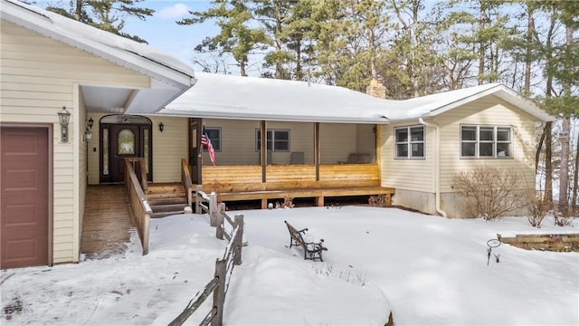 snow covered rear of property with covered porch and a chimney