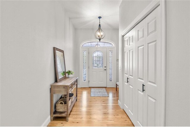 entryway with light wood-style flooring, a chandelier, and baseboards