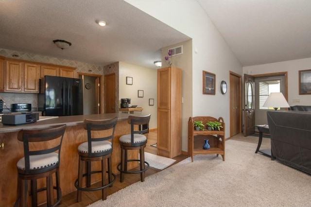 kitchen featuring freestanding refrigerator, visible vents, a peninsula, brown cabinetry, and a kitchen breakfast bar