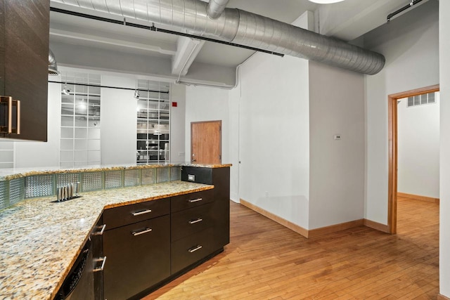 kitchen featuring dark brown cabinetry, visible vents, light wood-type flooring, and light stone counters