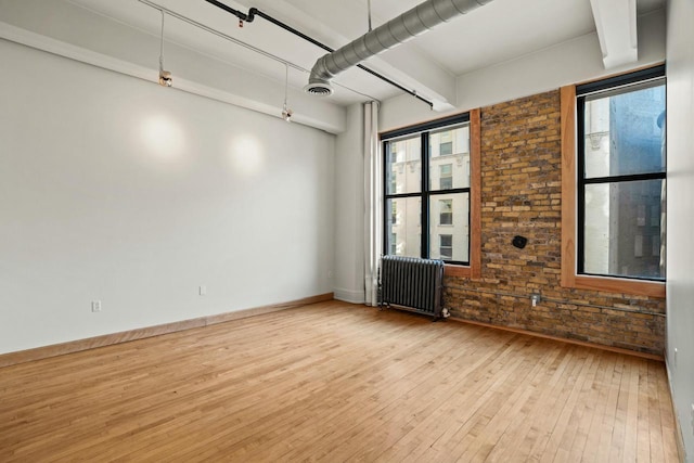 empty room featuring light wood-style flooring, visible vents, baseboards, radiator heating unit, and beamed ceiling