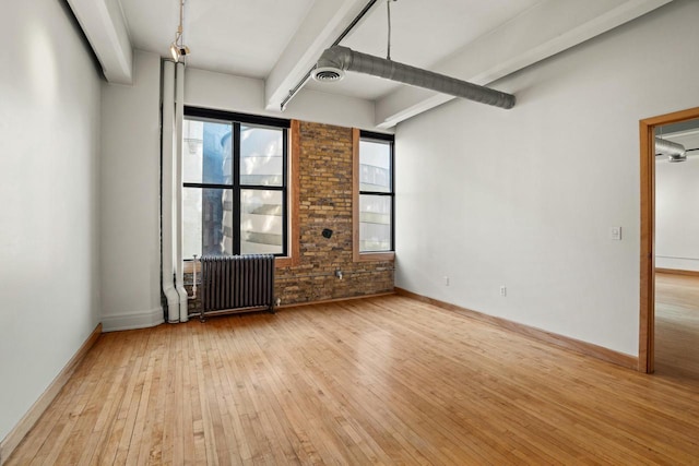 empty room featuring baseboards, light wood finished floors, radiator, and beamed ceiling