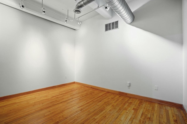 empty room with track lighting, visible vents, wood finished floors, and baseboards