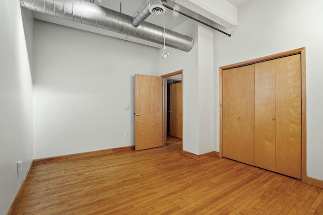 unfurnished bedroom with baseboards, light wood-style floors, a closet, and a high ceiling