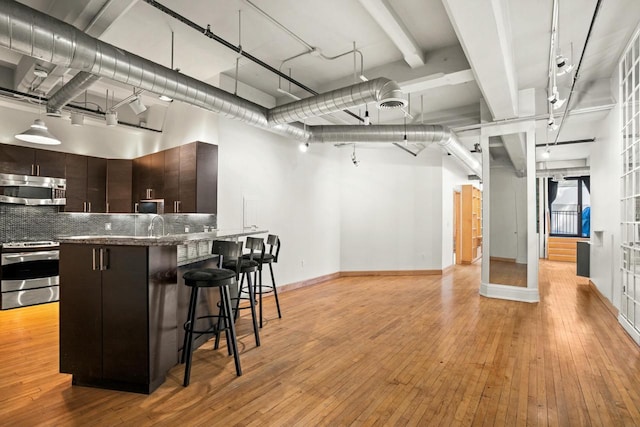 kitchen with dark brown cabinets, tasteful backsplash, a breakfast bar area, appliances with stainless steel finishes, and light wood-type flooring