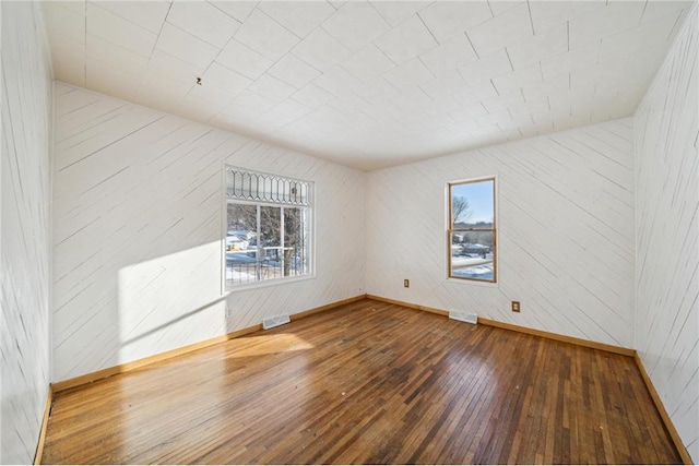 unfurnished room featuring baseboards, visible vents, and wood finished floors