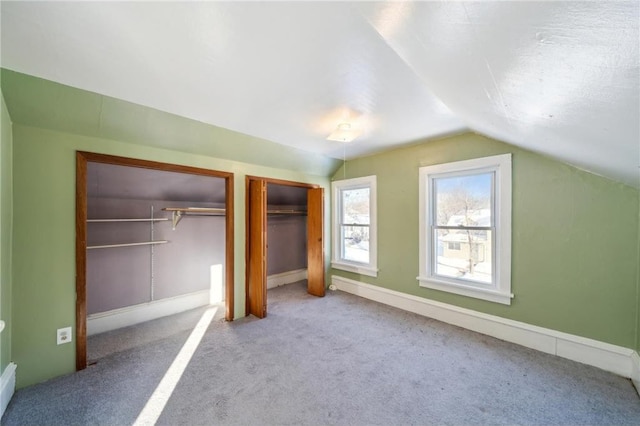 unfurnished bedroom featuring baseboards, vaulted ceiling, multiple closets, and carpet floors