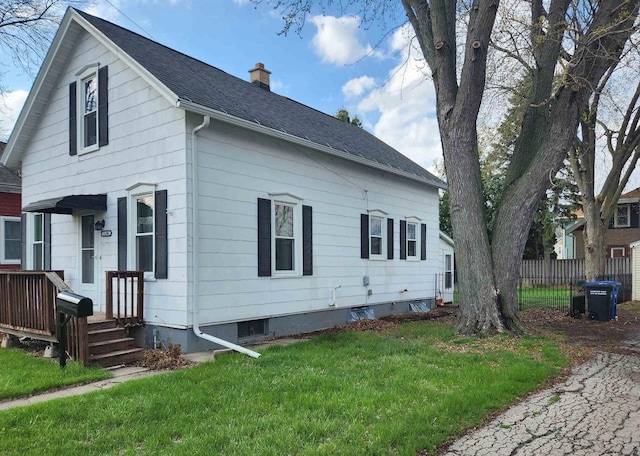 view of side of home featuring fence, roof with shingles, a yard, and a chimney