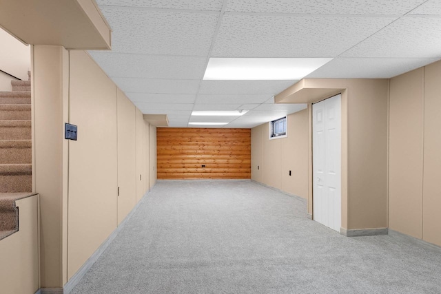 finished below grade area with light colored carpet, stairs, and a drop ceiling