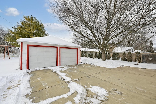 snow covered garage featuring fence and a garage