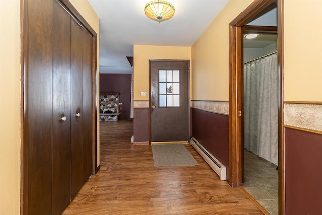 doorway with wainscoting, wood finished floors, and a baseboard heating unit