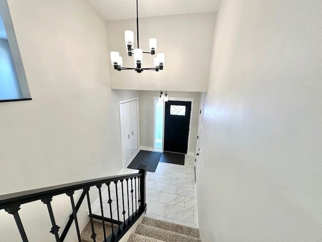 foyer entrance featuring a notable chandelier, marble finish floor, stairway, and baseboards