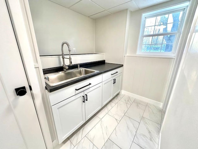 kitchen featuring white cabinets, a drop ceiling, dark countertops, marble finish floor, and a sink