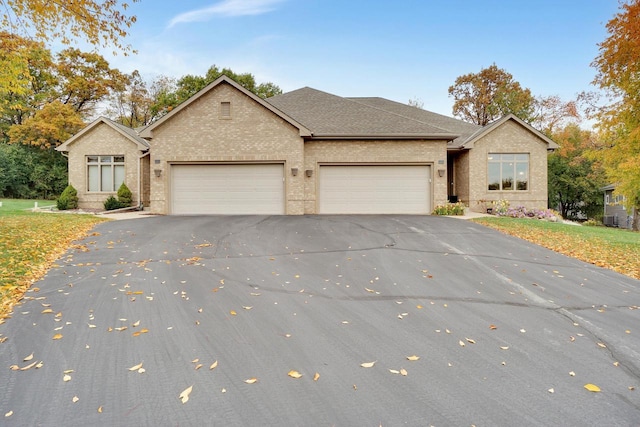 single story home with brick siding, a shingled roof, an attached garage, and driveway