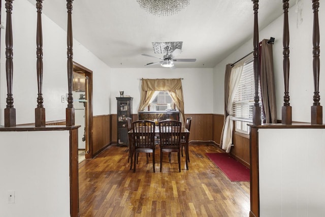 dining area with a wainscoted wall, dark wood-type flooring, a ceiling fan, and wood walls