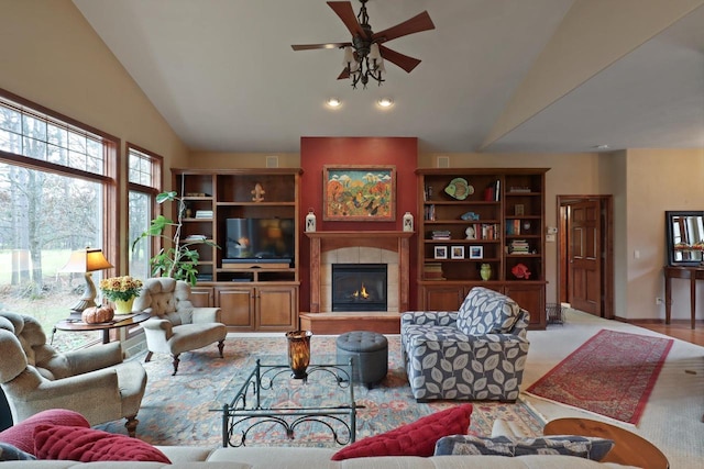 living area with a tiled fireplace, ceiling fan, and vaulted ceiling