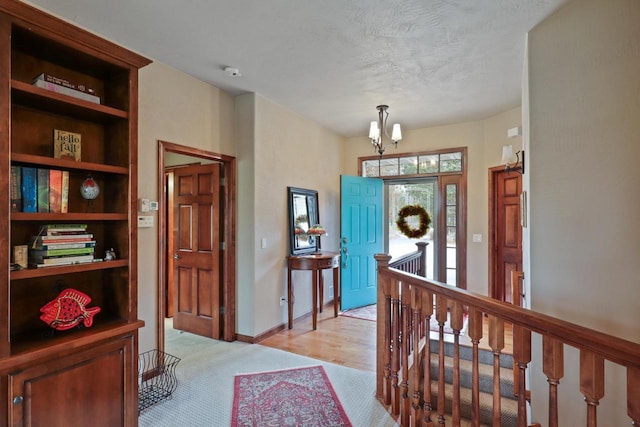 entrance foyer with baseboards, light colored carpet, a textured ceiling, and a notable chandelier