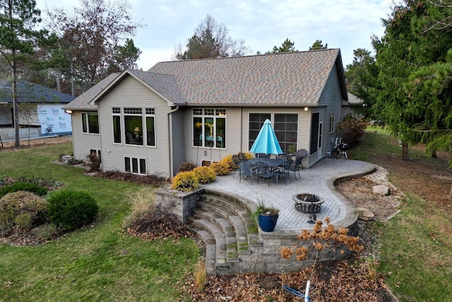 rear view of property with a shingled roof, an outdoor fire pit, a yard, and a patio area