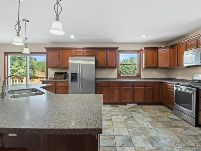 kitchen with stainless steel appliances, dark countertops, a sink, and pendant lighting