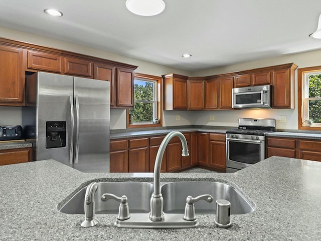 kitchen featuring appliances with stainless steel finishes, a sink, plenty of natural light, and light stone counters