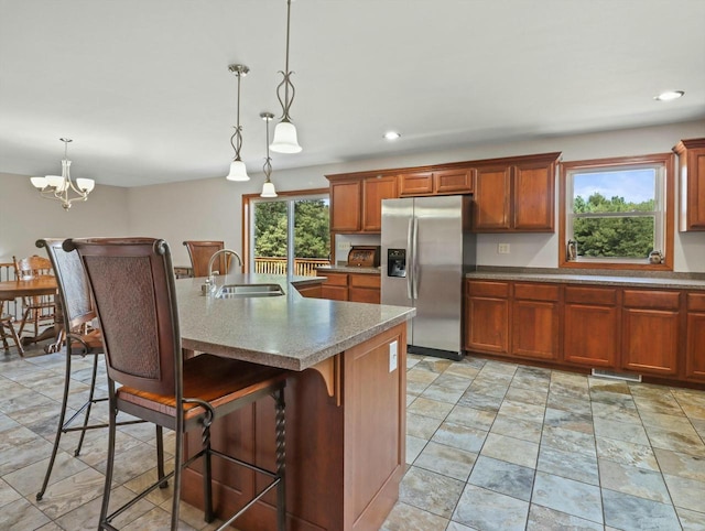 kitchen featuring hanging light fixtures, a sink, an island with sink, stainless steel fridge, and a kitchen bar