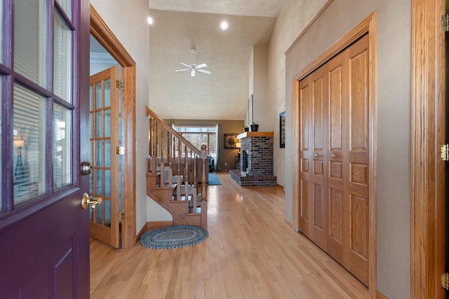 foyer with stairs, a brick fireplace, light wood-style flooring, and a ceiling fan