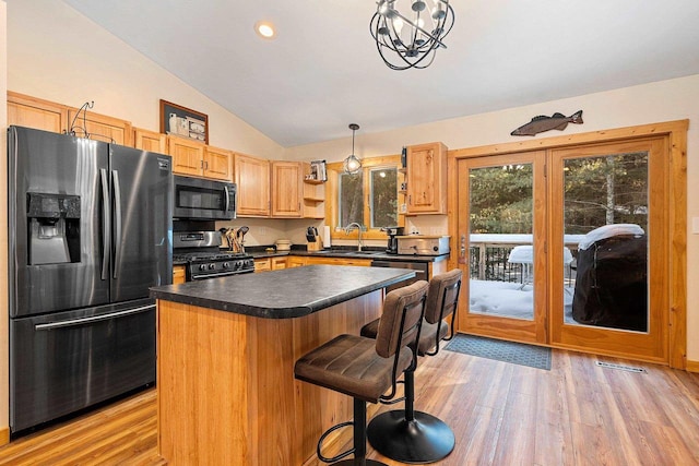 kitchen featuring lofted ceiling, stainless steel appliances, a kitchen island, hanging light fixtures, and dark countertops