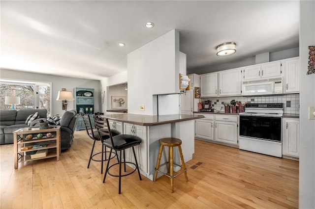 kitchen with white appliances, a breakfast bar, white cabinets, open floor plan, and dark countertops