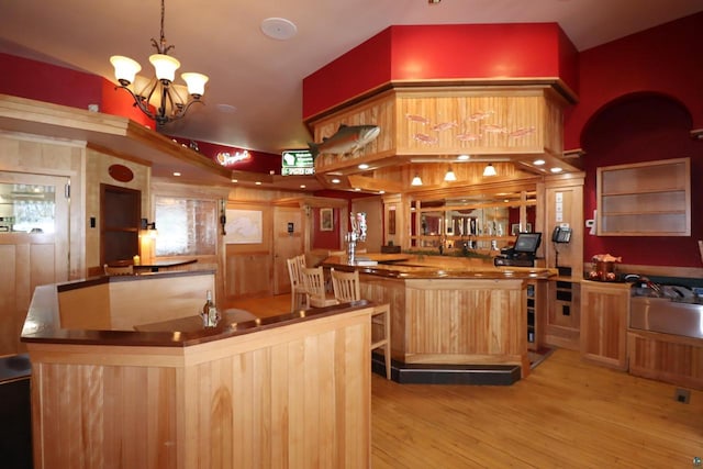 kitchen with light brown cabinetry, pendant lighting, light wood-style flooring, and an inviting chandelier