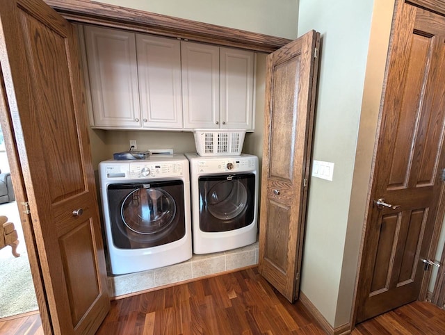 clothes washing area with dark wood finished floors, washing machine and clothes dryer, cabinet space, and baseboards