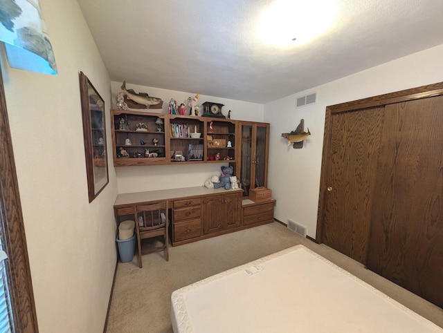 home office with built in desk, visible vents, and light colored carpet