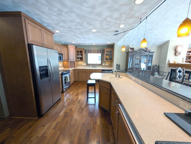 kitchen featuring glass insert cabinets, brown cabinets, a breakfast bar area, stainless steel appliances, and light countertops