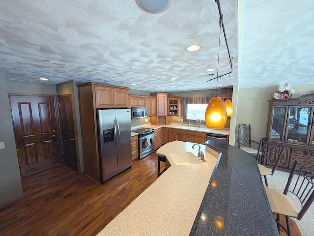 kitchen with decorative light fixtures, a sink, appliances with stainless steel finishes, brown cabinets, and glass insert cabinets