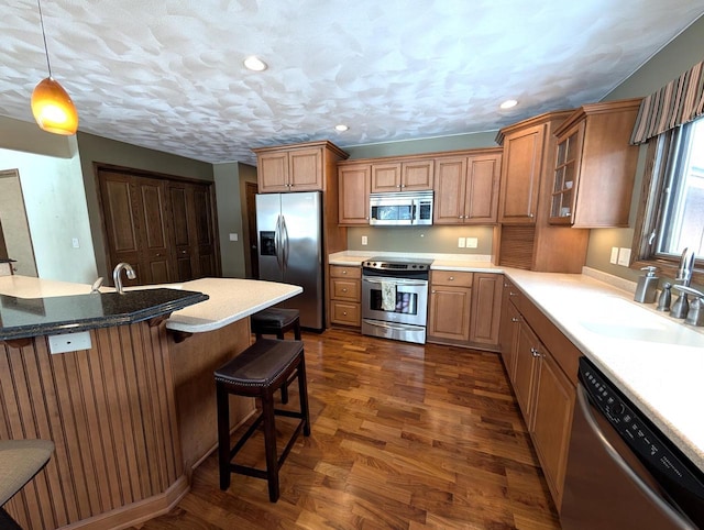 kitchen with decorative light fixtures, a breakfast bar area, stainless steel appliances, brown cabinetry, and glass insert cabinets