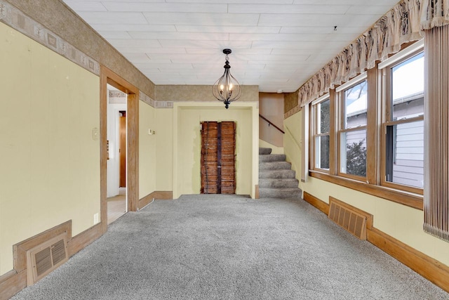 carpeted empty room with visible vents, a notable chandelier, and stairway