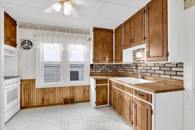 kitchen with wallpapered walls, white gas range oven, visible vents, a wainscoted wall, and a sink