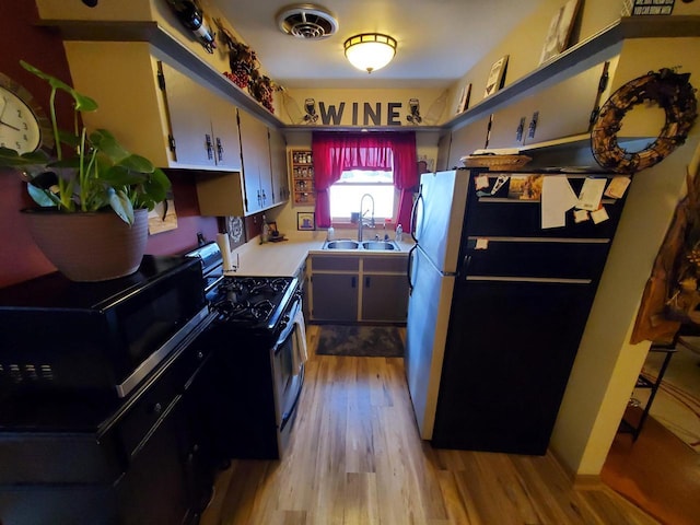 kitchen with freestanding refrigerator, light countertops, black microwave, a sink, and gas stove