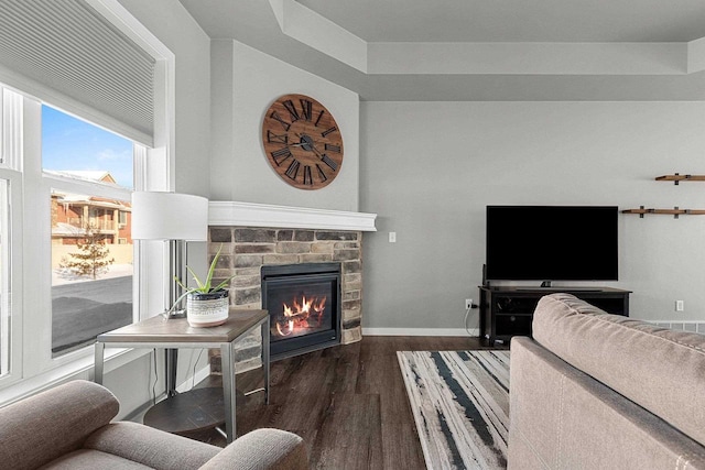 living area featuring a stone fireplace, dark wood-style flooring, and baseboards