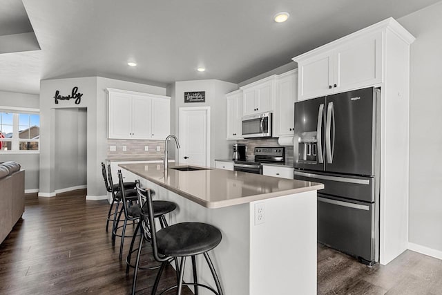 kitchen with a kitchen island with sink, white cabinetry, light countertops, appliances with stainless steel finishes, and a kitchen bar