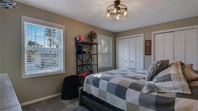 carpeted bedroom featuring baseboards, a chandelier, and two closets